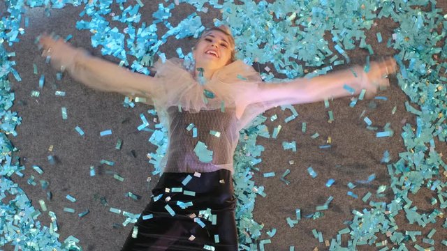 Crazy New Year's Eve. A beautiful woman lies on the floor and creates a snow angel out of blue confetti