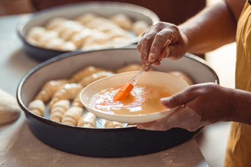 Female hands using brush to add egg topping on rolls. Process of making croissant rolls