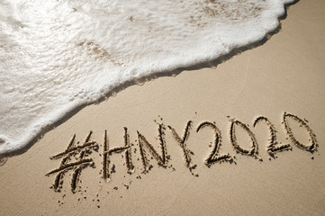 Modern New Year message with social media hashtag for 2020 handwritten in smooth sand with  oncoming wave on the beach