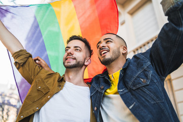 Gay couple embracing and showing their love with rainbow flag.