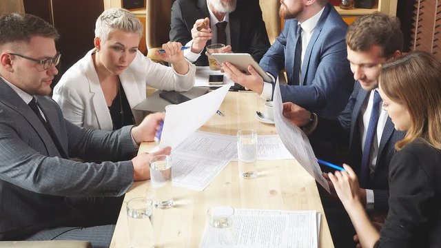 Businesspeople discussing issues together in small conference room during meeting at bright office against background wall with different alcohol drinks