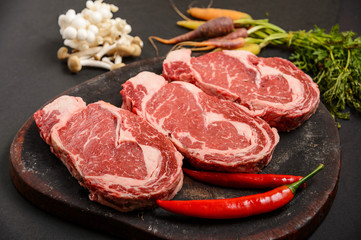 Three pieces of fresh beef meat with vegetables on wood, uncooked	