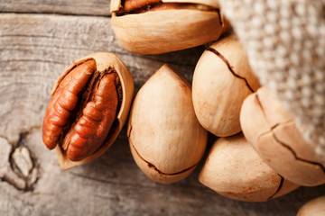 Fototapeta premium Pecans spill out of a bag on a wooden table, close-up. Peeled, in a shell.