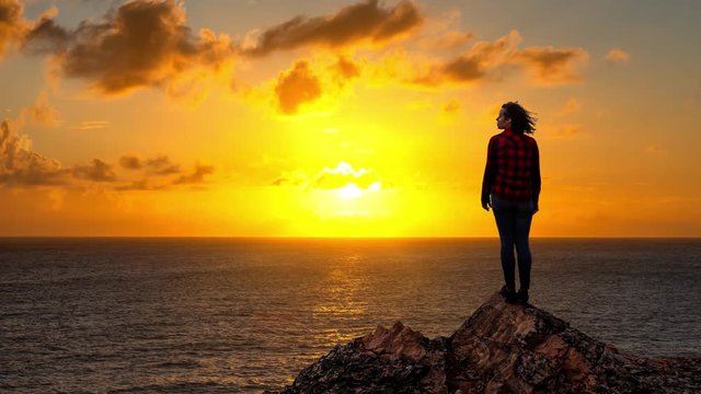 Cinemagraph, Seamless loop Animation. Adventurous Girl on a Rocky Ocean Coast enjoying the beautiful view of the Colorful Sunset. Image Composit. Adventure, Travel, Explore Concept.