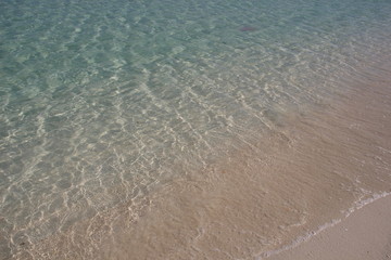 Calm sea water on white sand blinking in day sun