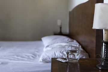 Water glass, a pack of tablets / pills and a bed in the blurred background