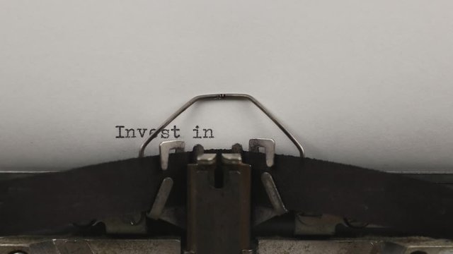 close-up typing a quote invest in yourself, old vintage typewriter with a sheet of paper 