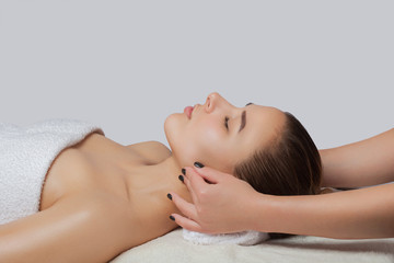 Fototapeta na wymiar Masseur makes a relaxing massage on the ears, face, neck, shoulders and collarbones of a young beautiful woman in a spa. Cosmetology and massage concept.