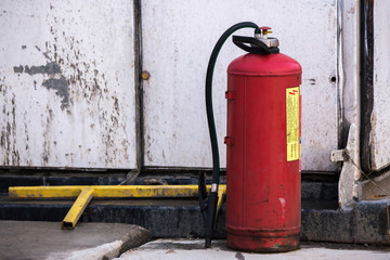 Red Fire extinguisher standing next to a white damaged building