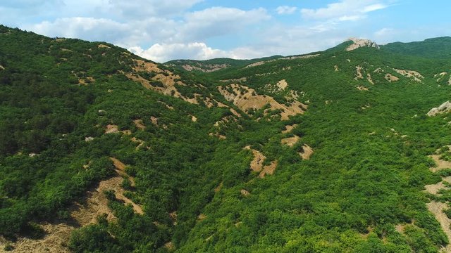 Aerial view of picturesque mountains covered with green trees and against blue cloudy sky in sunny summer day. Shot. Beautiful mountains scenery