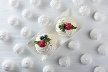 Dessert Pavlova with raspberries, blueberries and mint on a white table.