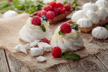Pavlova and small meringues on a rustic wooden background.