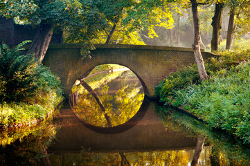 Stone old bridge reflection in the form of a circle in water of a canal in a park, Den Bosch, The Netherlands - obrazy, fototapety, plakaty