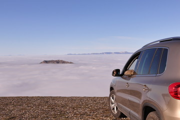 Fototapeta na wymiar MAN WITH A CAR HIGH ON A MOUNTAIN LOOKING AT A VALLEY COVERED WITH A DENSE LAYER OF CLOUDS