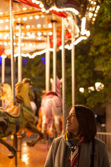 young woman standing next to a vintage carousel at night