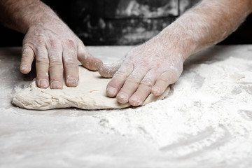 Hands of male baker preparing yeast dough with white flour dust on black background, scoop out for...