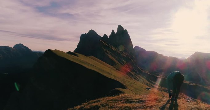 Aerial View. Young man in sport trail clothes stretching on Seceda mountain peak at sunrise. Puez Odle, Trentino, Dolomites, Italy.