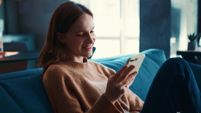 Shoot of cute caucasian young woman scrolling, surfing the internet, watching contents or bloggs and smiling.