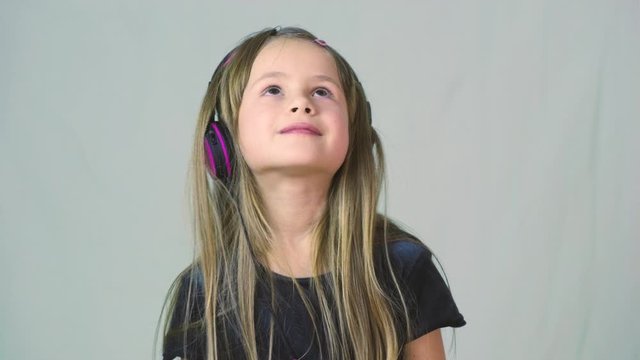Pretty smiling cild girl listening to music in big pink earphones.