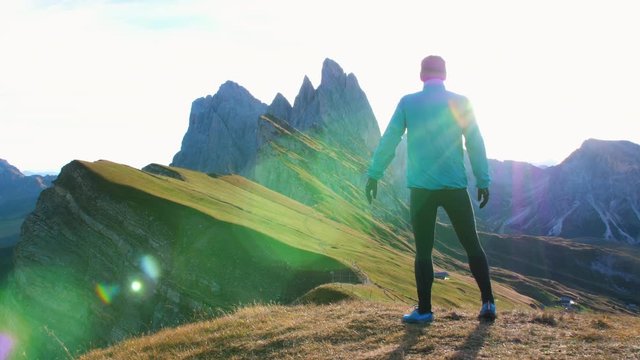Young man in sport trail clothes running on Seceda mountain peak at sunrise. Puez Odle, Trentino, Dolomites, Italy.