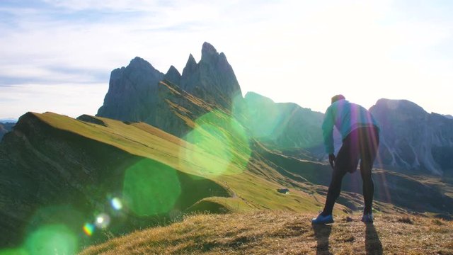 Young man in sport trail clothes stretching on Seceda mountain peak at sunrise. Puez Odle, Trentino, Dolomites, Italy.