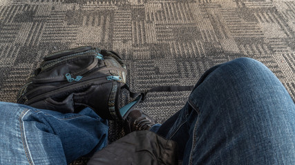 Lower section of a person waiting with backpack on a bench in the airport