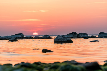 Fototapeta na wymiar Beautiful orange and red sunset over the ocean with rocks in the forground