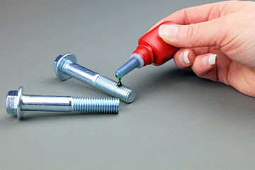 A Female Engineers Hand Applying A Drop Of Thread Locking Fluid To The Threads Of A Bolt.
