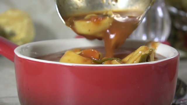 Ladling fresh hot tortellini soup into a bowl slow motion
