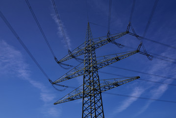A power pole stands with many cables in front of a blue sky with few clouds when the sun is shining...