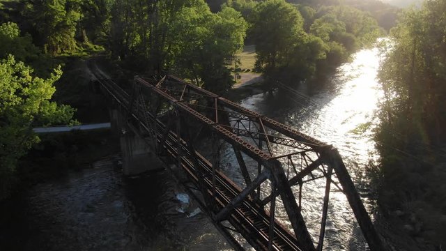 Forested railroad trestle bridge over river at sunset 4k aerial Mavic 2 Zoom. Panning over bridge and tilt down
