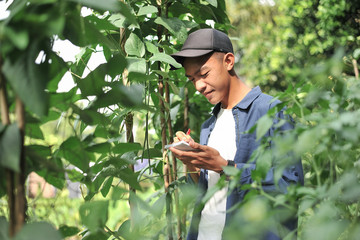 Portrait of smiling young Asian farmer man writing on the small notebook. Happy young Asian farmer at the garden