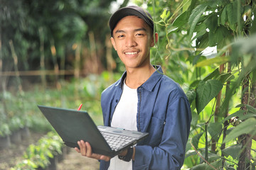 Young Asian farmer man holding laptop at the garden