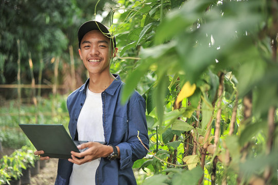 Young Asian farmer man holding laptop at the garden