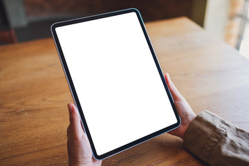 Mockup image of a woman holding black tablet pc with blank white screen on wooden table