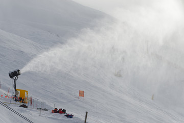 A snow canon shoots man made snow into the sky over a ski field