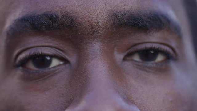 Close up portrait of black male's eyes opening before smiling to camera, in slow motion