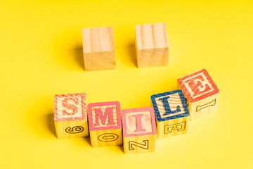 Happiness concept: wooden blocks forming a smiling face against yellow background.  Copy space for text