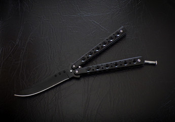 Butterfly knife on a black leather background. Balisong knife.