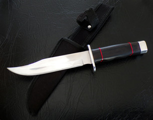 Hunting knife on a black leather background. Bowie knife with scabbard close-up. A handmade knife. - obrazy, fototapety, plakaty