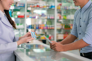 Confident Asian young female pharmacist with a lovely friendly smile and explaining capsule...