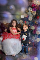 girl in elegant dress near the Christmas tree with her brother