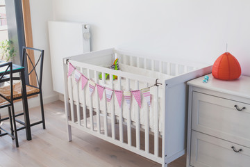 white baby bed crib in child room interior, decorated with paper handmade garland, scandinavian style design
