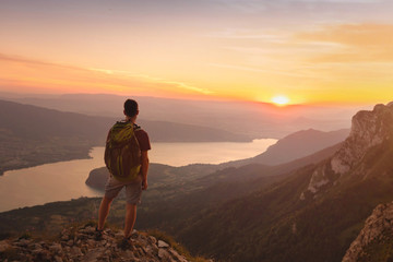 Fototapeta premium adventure travel with backpack, hiking outdoor in Alps near Annecy lake, man standing on top of mountain at sunset
