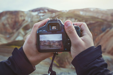 landscape travel photographer hands holding camera, taking photo of mountains