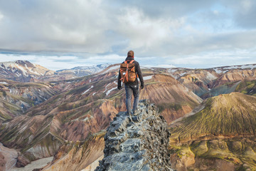 adventure travel, hiking in Iceland with backpack, tourist looking at colorful landscape of Landmannalaugar - obrazy, fototapety, plakaty