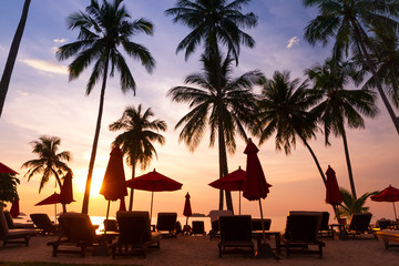 tropical beach at sunset, tourist hotel with silhouettes of palm trees and deckchairs, vacation in luxury resort