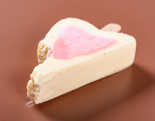 side view half eaten strawberry flavor popsicle on a brown background