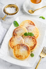 Cottage cheese pancakes on a white rectangular dish on a marble table. Curd fritters with tea for breakfast. Syrniki - a traditional dish of Russia, Belarus, Ukraine. Selective focus