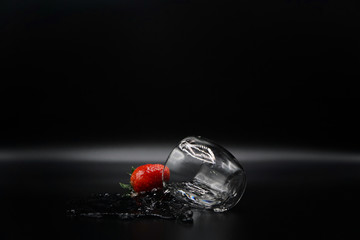 A strawberry drops out off a glass of clear water causing water splash on the black background